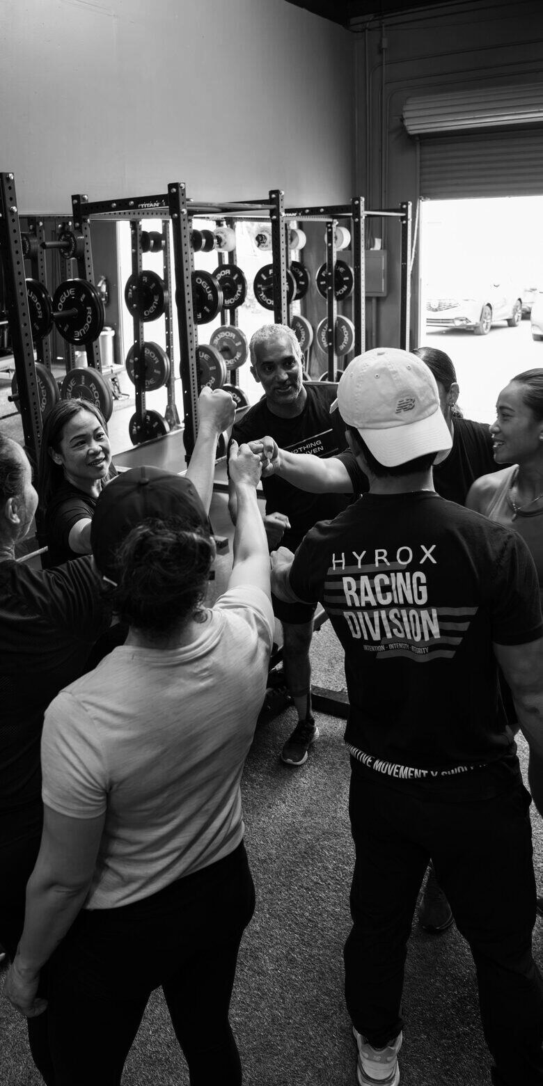 A coach and seven clients fist-bump in a circle after a Hyrox training session — desaturated