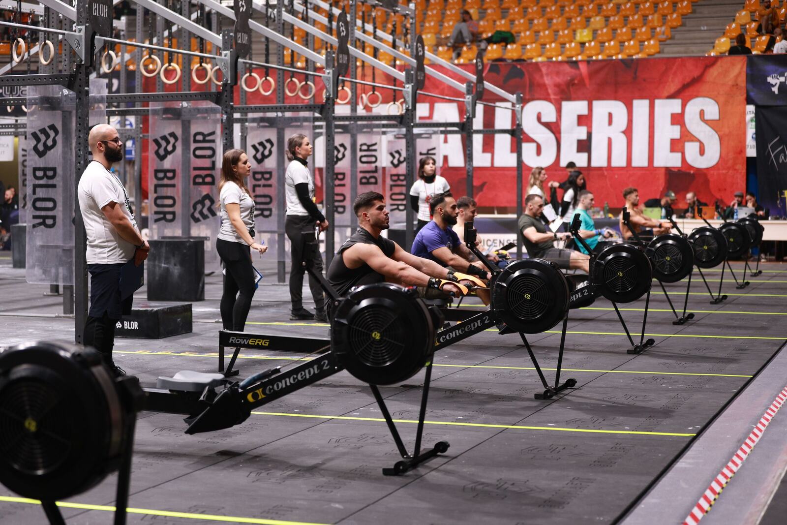 A row of rowing ergs with a whole heat working down the line, judges standing over them